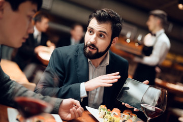 Meeting with chinese businessmen in restaurant. Man is showing tablet.