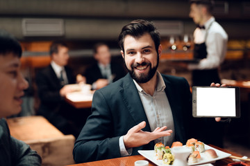 Meeting with chinese businessmen in restaurant. Man is showing tablet.