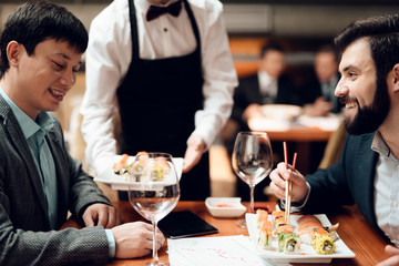 Meeting with chinese businessmen in restaurant. Waiter brings sushi to table.