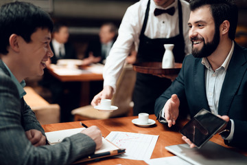 Meeting with chinese businessmen in restaurant. Waiter brings coffee.