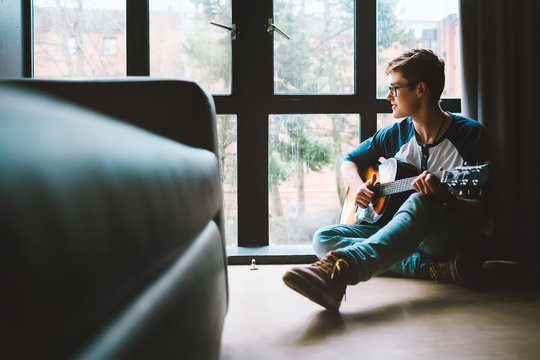 Boy with guitar sits on the floor at cozy home, moody day light