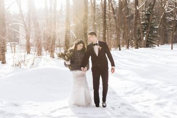 Fototapeta na wymiar Bride and groom among snowy landscape. Bride and groom are holding hands and walk the snowy road.