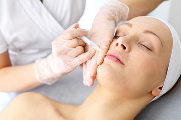 Modelowanie ust wypełniaczem Kosmetyczka ostrzykuje  twarz kobiety podczas zabiegu odmładzającego w klinice piękności.