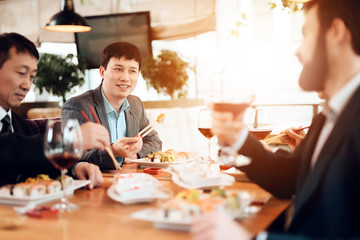 Meeting with chinese businessmen in restaurant. Men are eating sushi.