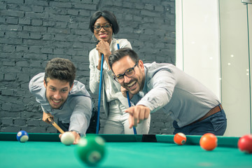 Cheerful business people playing billiards during office break.