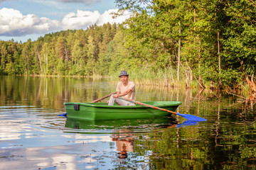 Fisherman with fishing rods is fishing in a wooden boat against background of beautiful nature and lake or river. Camping tourism relax trip active lifestyle adventure concept