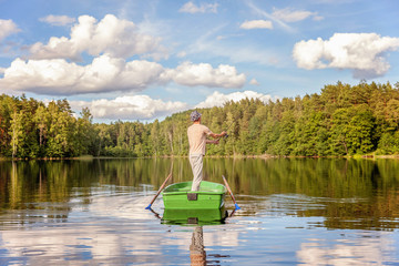 Fototapeta na wymiar Fisherman with fishing rods is fishing in a wooden boat against background of beautiful nature and lake or river. Camping tourism relax trip active lifestyle adventure concept