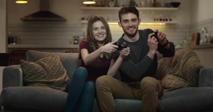Cute couple shove and elbow each other on the couch as they play a video game at home