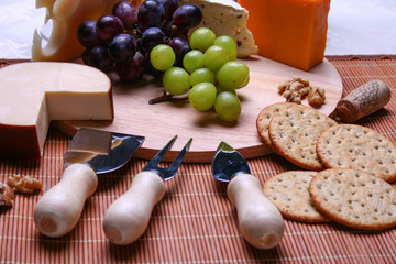 Still life 3 types of cheese roquefort cheese, red and green grapes, crackers, walnuts, cheese utensils on wooden plate