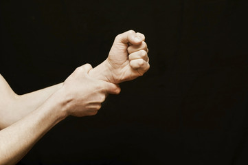 A hand on a black background is squeezed into a fist and wants to hit someone, and the other hand holds an aggressive hand and holds it away from violence