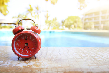 Red retro and vintage alarm clock with metal bell and hanger on wood floor near swimming pool