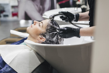 Beautiful young woman to hairdresser while washing head in hair salon