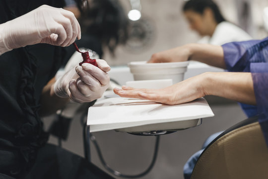 Young woman while applying red nail polish during a manicure by the beautician