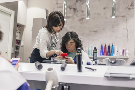 Young hairdresser talking with her client after a styling looking at the smartphone in a beauty salon