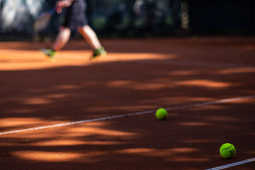 Tennis ball on a court in the foreground. Person blurred in the background playing