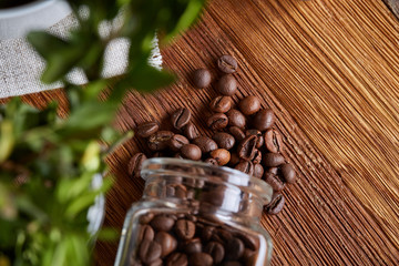 Roasted coffee beans get out of overturned glass jar on homespun tablecloth, selective focus, side view