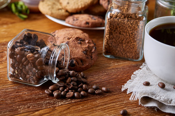 Coffee cup, jar with coffee beans, cookies over rustic background, selective focus, close-up, top view
