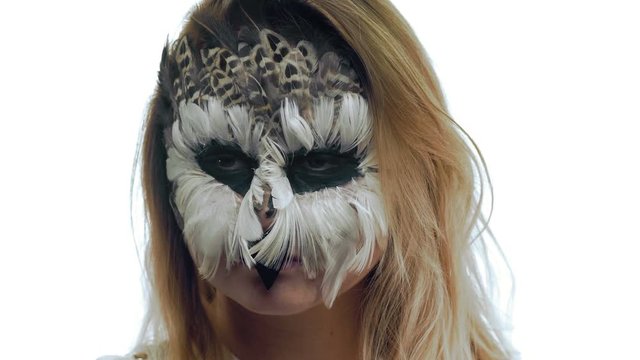 Close-up, a girl with a make-up from feathers of a bird blinks her eyes imitating an owl