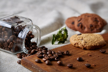 Roasted coffee beans get out of overturned glass jar on homespun tablecloth, selective focus, side view