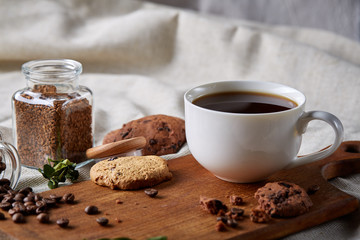 Coffee cup, jar with coffee beans, cookies over rustic background, selective focus, close-up, top view