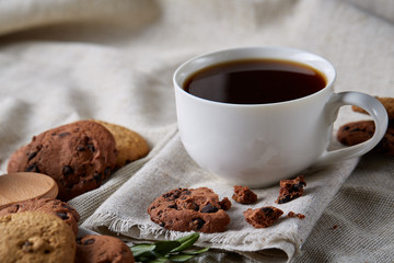 Morning coffee in white cup, chocolate chips cookies on cutting board close-up, selective focus
