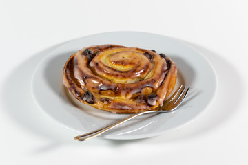 Rosinenschnecke mit Zuckerguss auf einem weißen Kuchenteller mit Kuchengabel isoliert vor weißem Hintergrund