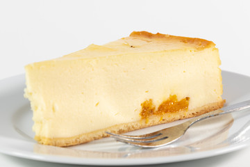 Ein Stück Käsekuchen gefüllt mit Mandarinen neben einer Kuchengabel auf einem weißen Kuchenteller isoliert auf weißem Hintergrund