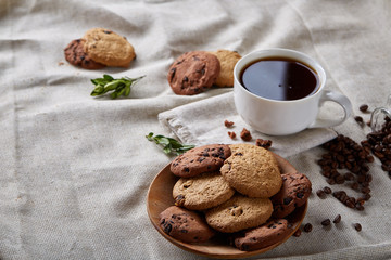Morning coffee in white cup, chocolate chips cookies on cutting board close-up, selective focus