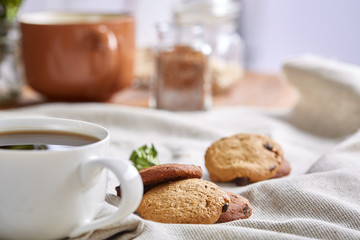 Morning coffee in white cup, chocolate chips cookies on cutting board close-up, selective focus