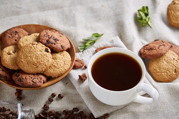 Morning coffee in white cup, chocolate chips cookies on cutting board close-up, selective focus