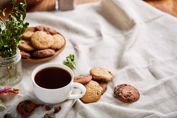 Morning coffee in white cup, chocolate chips cookies on cutting board close-up, selective focus