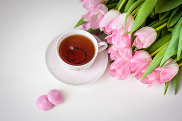 Bouquet of tulips and cup of tea on white background. Holiday card. Soft focus, copy space, top view. Spring concept.