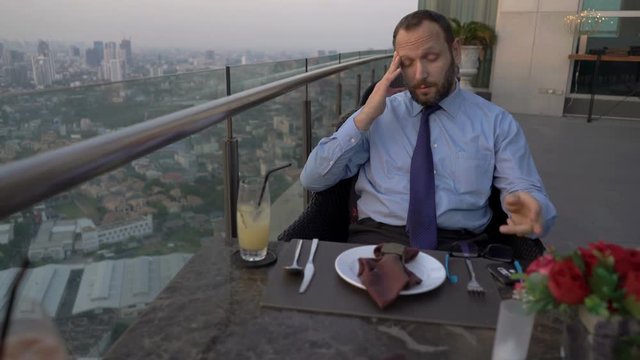 Businessman sitting on the rooftop and having painful headache
