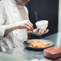 Restaurant Chef cook preparing salmon filet and crambling salad on the fish.