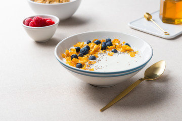 Healthy breakfast. Corn flakes with yogurt, blueberries and chia seeds. Served with maple syrup and raspberries on beige fabric background.