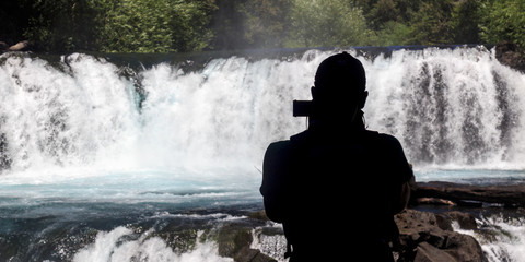 Silhouette of a person filming a cascade