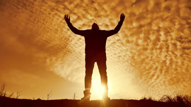 Silhouette of a man with hands raised in the sunset concept for religion, worship, prayer and praise. silhouette of a man at sunset nature of a hand in the sunlight party. freedom and victory concept