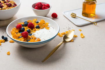 Healthy breakfast. Corn flakes with yogurt, almonds, blueberries, raspberries and chia seeds in white bowl.