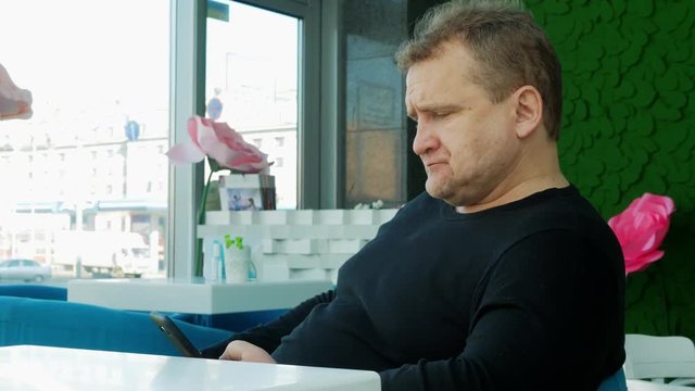 4k Middle age man with mobile phone siting alone in cafe at lunch