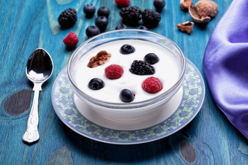 A bowl of yogurt with blueberries redcurrants blackberries and walnuts