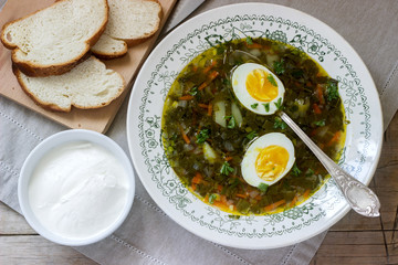 Vegetarian sorrel soup with egg, served with sour cream and bread. Rustic style.