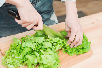 Close-up Female hands chopping a green plant salad cooking salad from vegetables on a wooden cutting board at home. The concept of vegetarianism and healthy lifestyles
