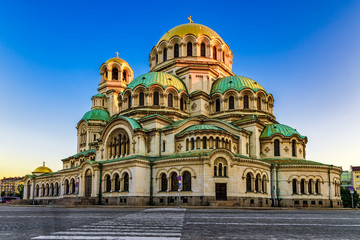 Fototapeta na wymiar Sunlit domes of Alexander Nevsky Cathedral (completed 1912) against clear blue sky and zebra crossing leading towards the church, Sofia, Bulgaria