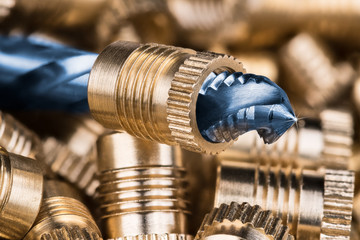 Threaded insert close-up and spiral flute tap. Beautiful detail of the cutting tool for threading with rays on tip and blurred background of bronze thread inserts. Idea of machining, build, metalwork.