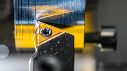 Detail of tool bit when machining on a lathe. Beautiful industrial background with turning workpiece, wavy metal swarf and reflection of triangular yellow cutter tool.