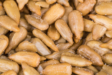 Close-up of salted sunflower seeds as a culinary background. Helianthus. Decorative texture from the pile of roasted grains sprinkled by crystals of kitchen salt.