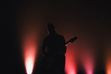 Rock band performs on stage. Guitarist plays solo. silhouette of guitar player in action on stage in front of concert crowd.