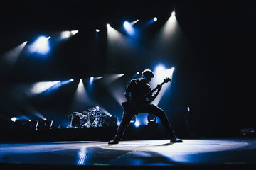 Rock band performs on stage. Guitarist plays solo. silhouette of guitar player in action on stage in front of concert crowd.