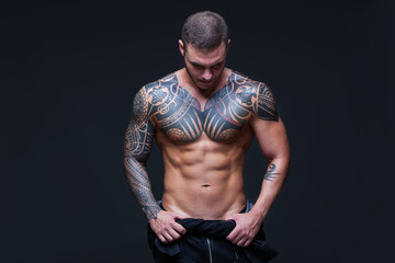 The man with a muscular naked torso with tattoos on the dark background. ABS