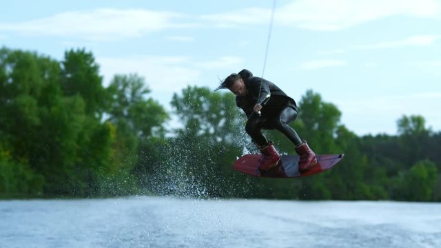 Wake board rider jumping high over water. Dangerous trick over river. Extreme water sports. Action time in summer. Wakeboarder making tricks. Extreme wakeboarding sport. Wake surfing rider on water